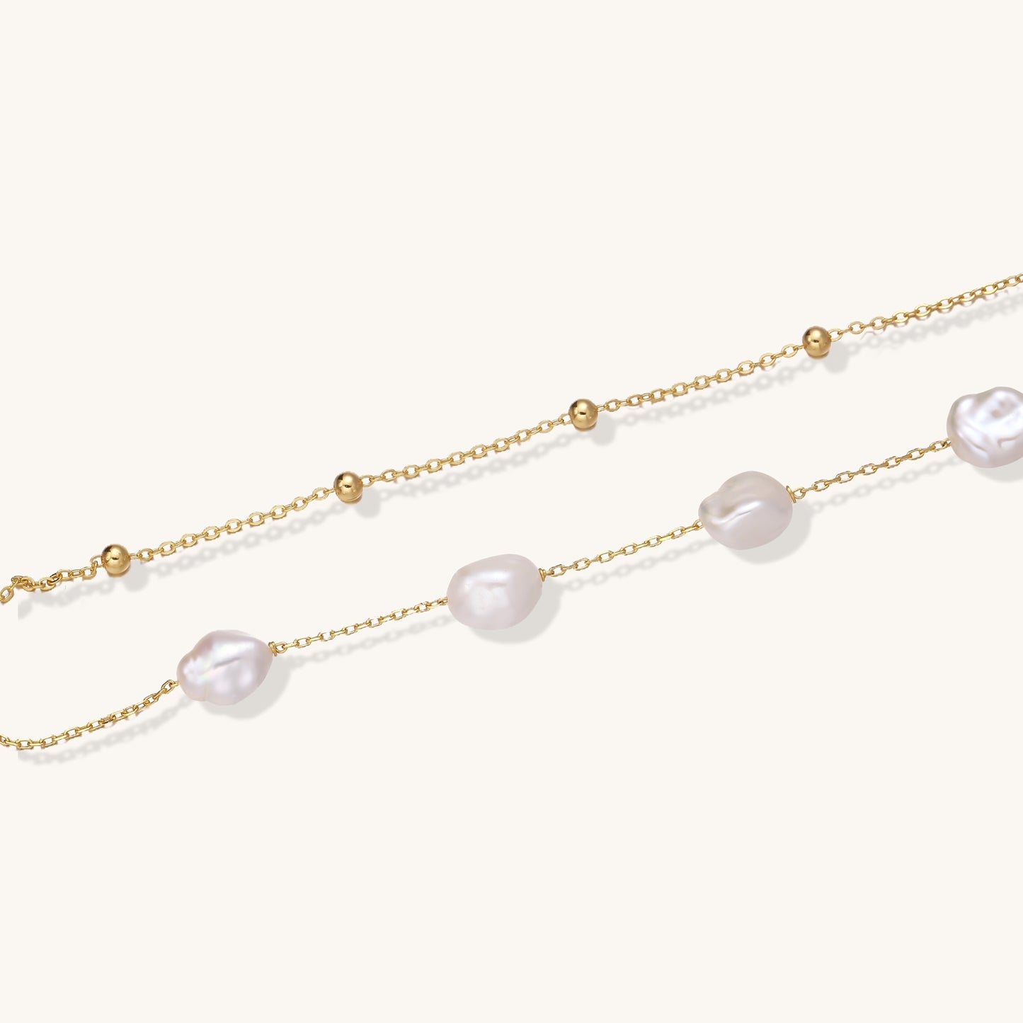 Delicate multi-layered gold-plated bracelet with irregular baroque pearls and freshwater pearls on cream background.