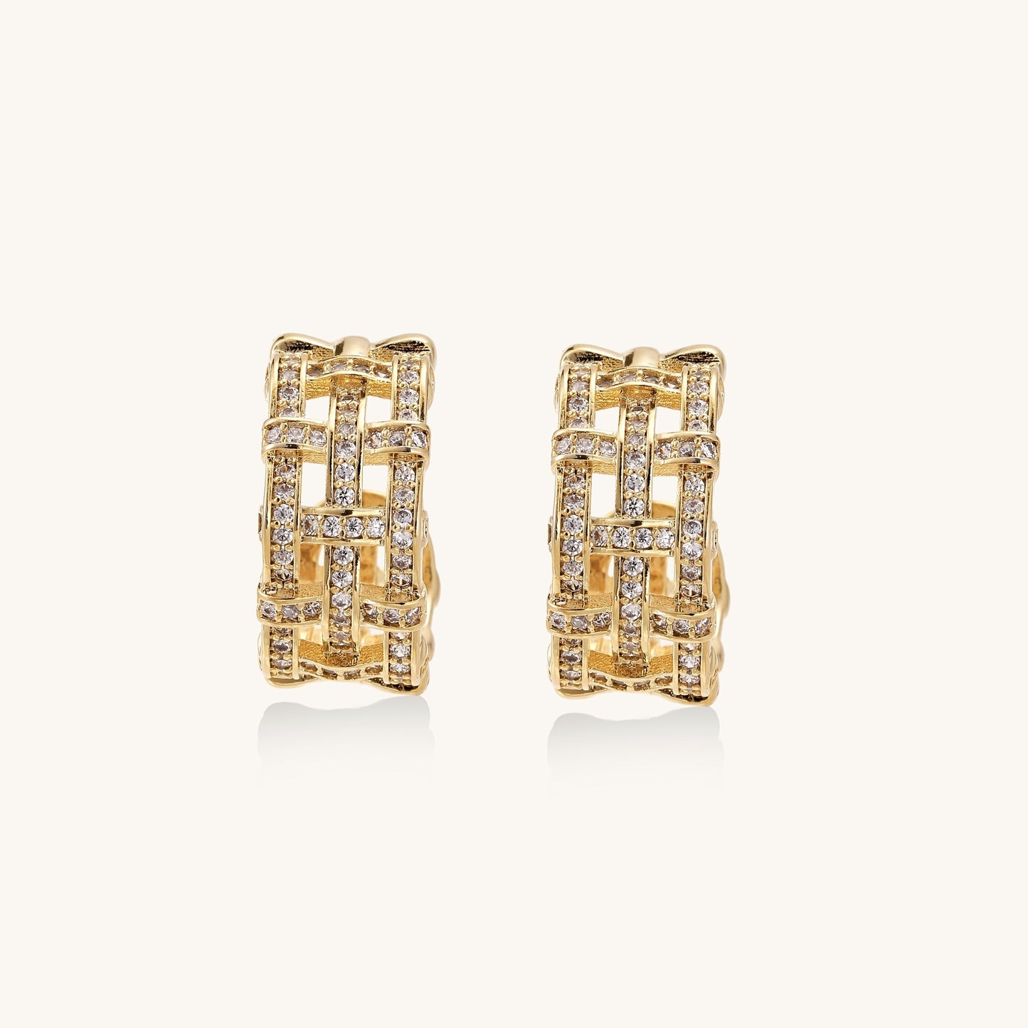 Close-up of geometric gold-plated hoop earrings with crystal pave in intricate lattice pattern on neutral background.