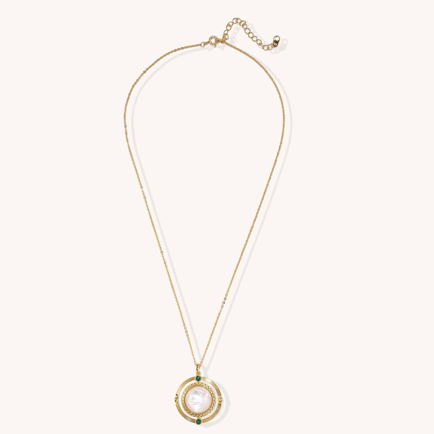 Gold-plated pendant necklace with circular orbital design, iridescent mother-of-pearl center and green zirconia accents