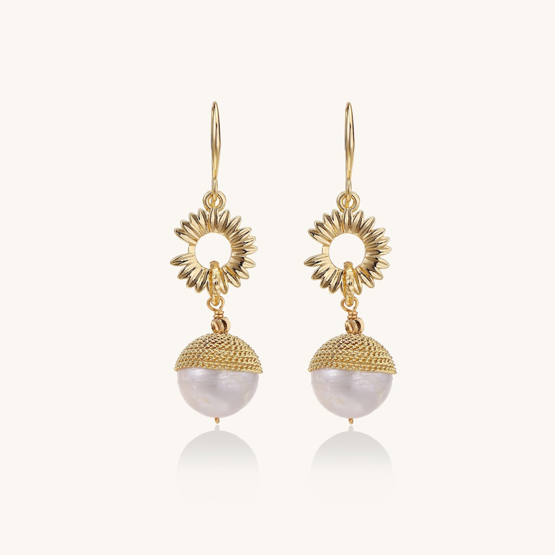 Gold-plated sunburst flower earrings with baroque pearl drops and textured metal caps on neutral background.