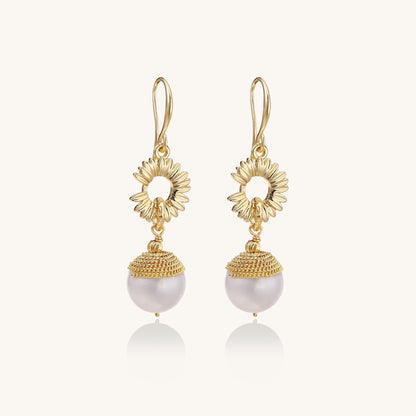 Gold-plated sunburst flower earrings with baroque pearl drops and textured metal caps on neutral background.