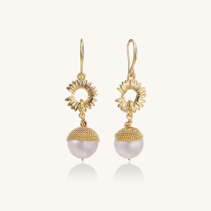Gold-plated sunburst flower earrings with baroque pearl drops and textured metal caps on neutral background.