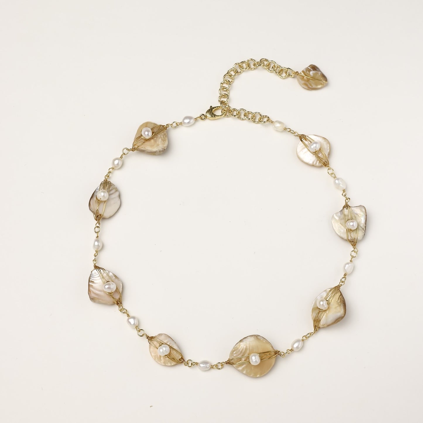 Delicate gold chain bracelet featuring iridescent shell charms with freshwater pearls on white background.