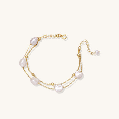 Delicate multi-layered gold-plated bracelet with irregular baroque pearls and freshwater pearls on cream background.