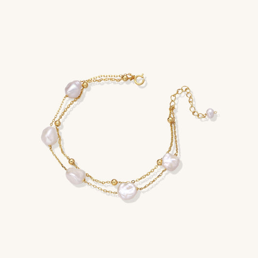 Delicate multi-layered gold-plated bracelet with irregular baroque pearls and freshwater pearls on cream background.
