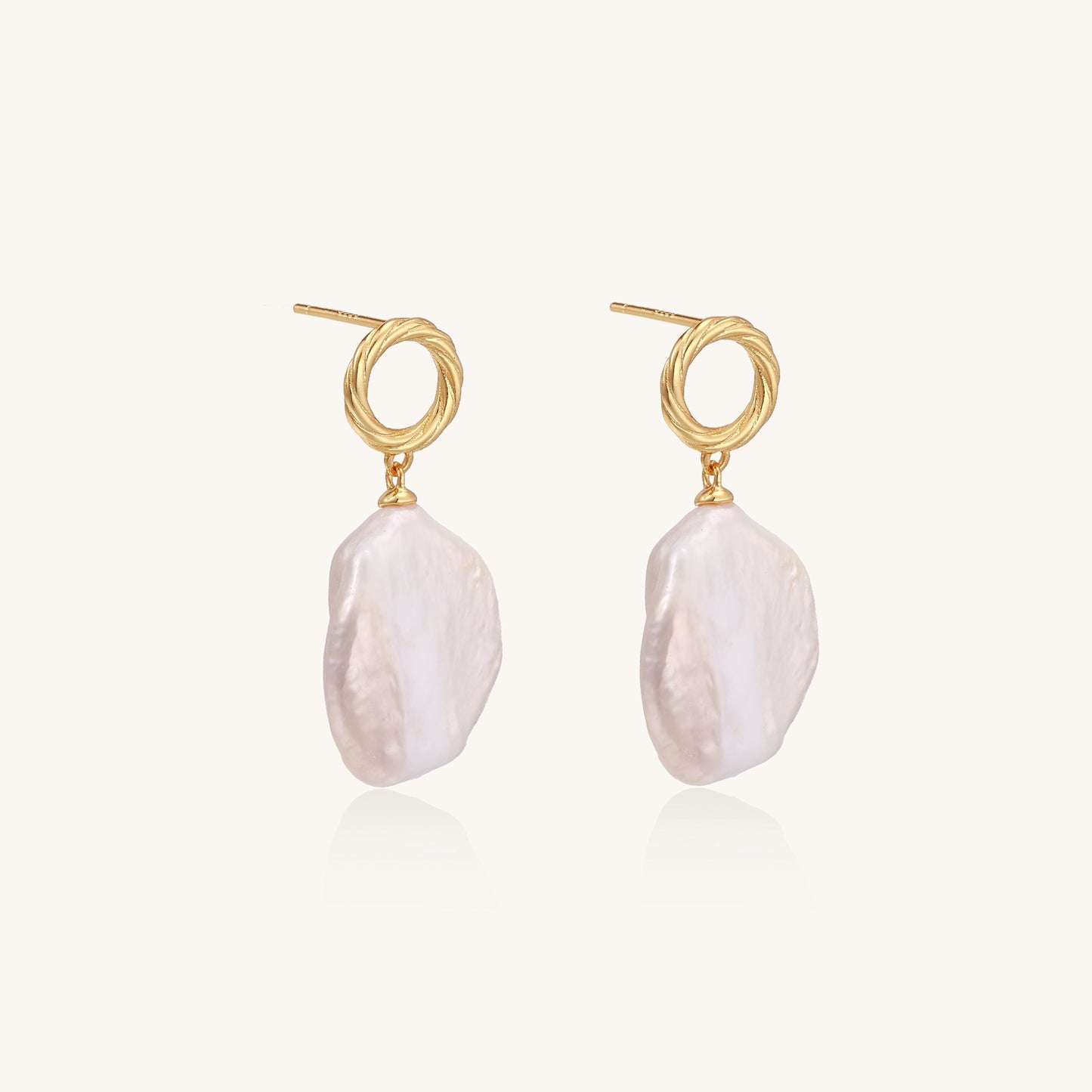 Gold-plated twisted stud earrings with large blush baroque pearls hanging elegantly on white background.