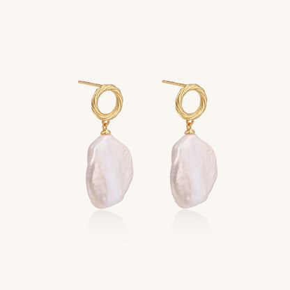 Gold-plated twisted stud earrings with large blush baroque pearls hanging elegantly on white background.