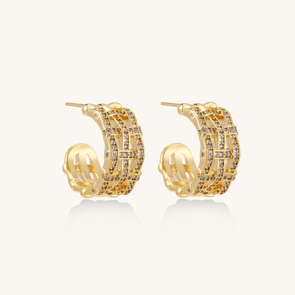 Close-up of geometric gold-plated hoop earrings with crystal pave in intricate lattice pattern on neutral background.