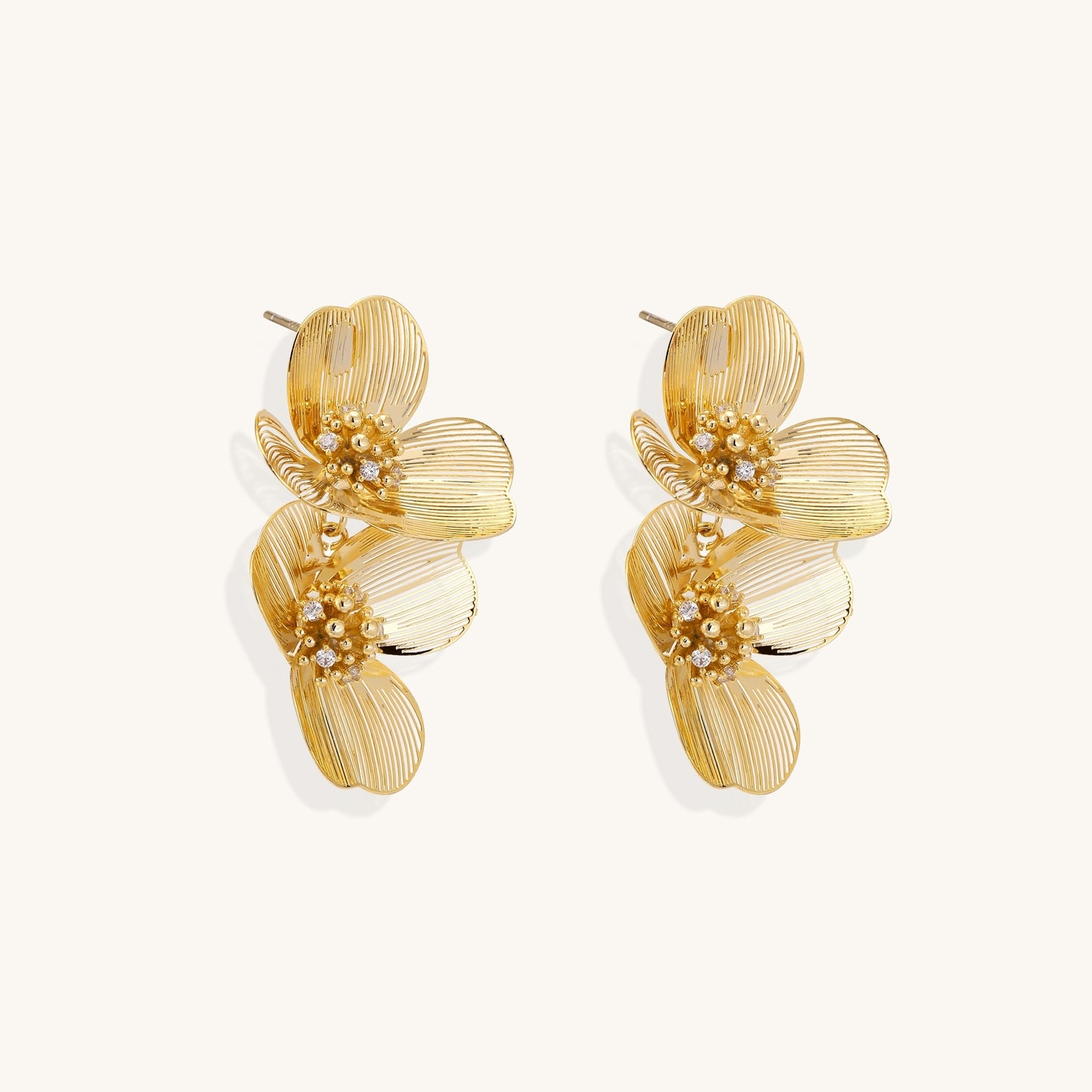 Layered gold-plated floral stud earrings with textured petals and crystal-accented centers on white background.