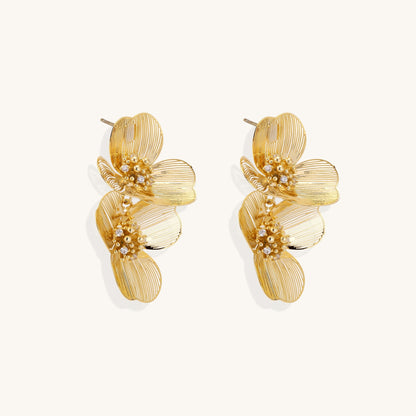 Layered gold-plated floral stud earrings with textured petals and crystal-accented centers on white background.