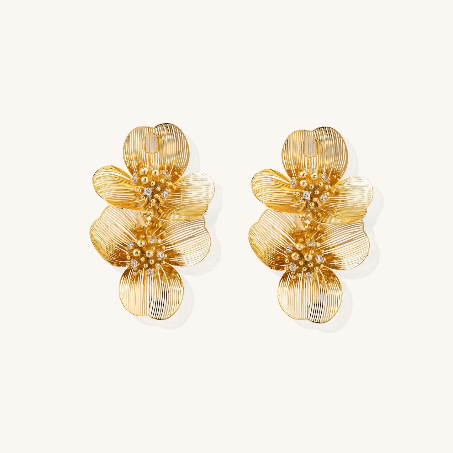 Layered gold-plated floral stud earrings with textured petals and crystal-accented centers on white background.