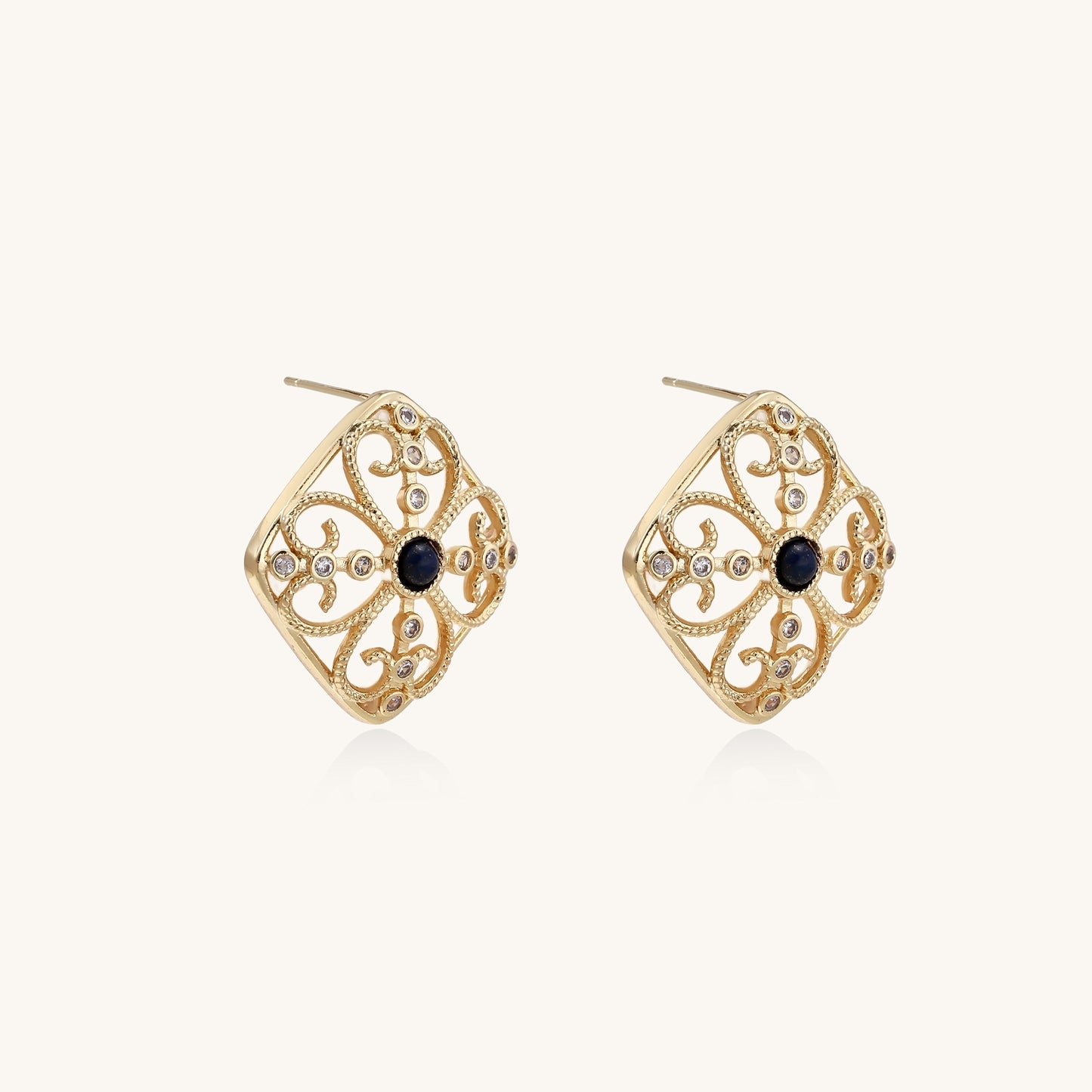 Ornate 18K gold plated stud earrings with intricate filigree design and central lapis lazuli stones on cream background.