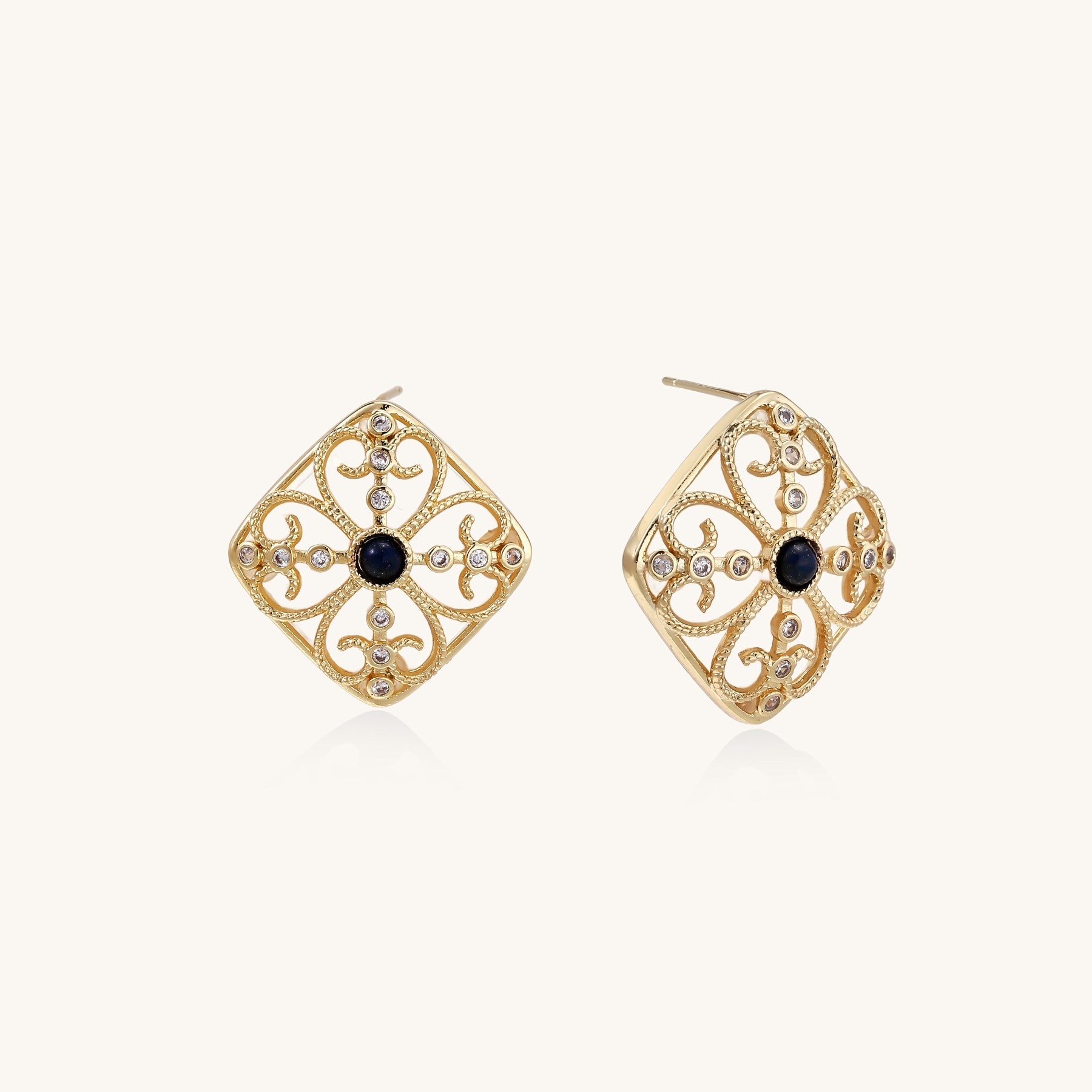 Ornate 18K gold plated stud earrings with intricate filigree design and central lapis lazuli stones on cream background.