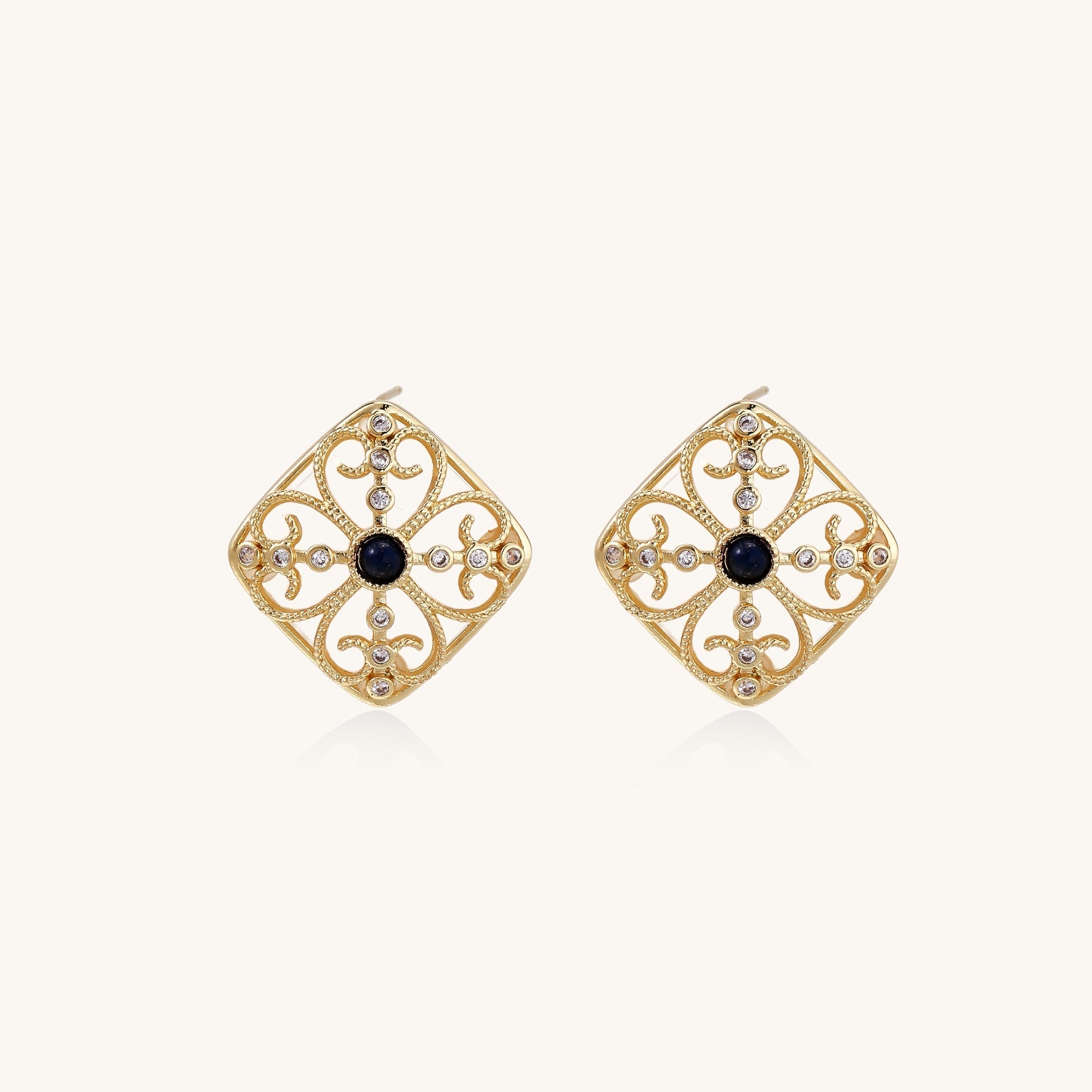 Ornate 18K gold plated stud earrings with intricate filigree design and central lapis lazuli stones on cream background.