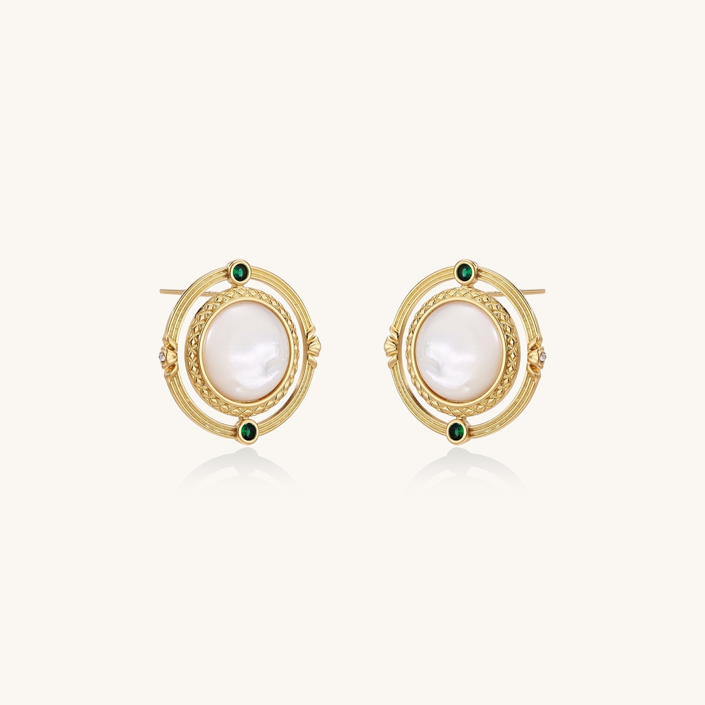 Close-up of gold-plated circular earrings with white mother-of-pearl centers and green zirconia accents on cream background.