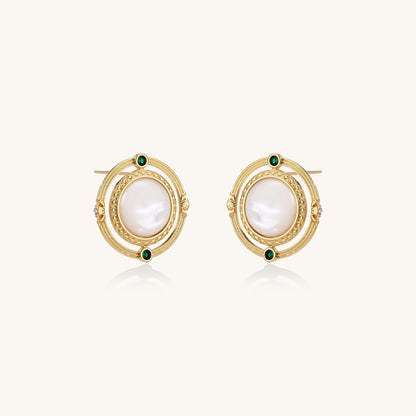 Close-up of gold-plated circular earrings with white mother-of-pearl centers and green zirconia accents on cream background.