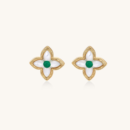Dainty gold-plated quatrefoil stud earrings with white mother-of-pearl petals and green gemstone centers on beige background.