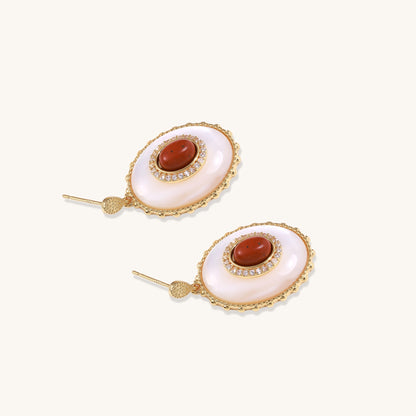 Gold-plated drop earrings with oval mother-of-pearl stones, central red gemstones, and crystal accents on white background.