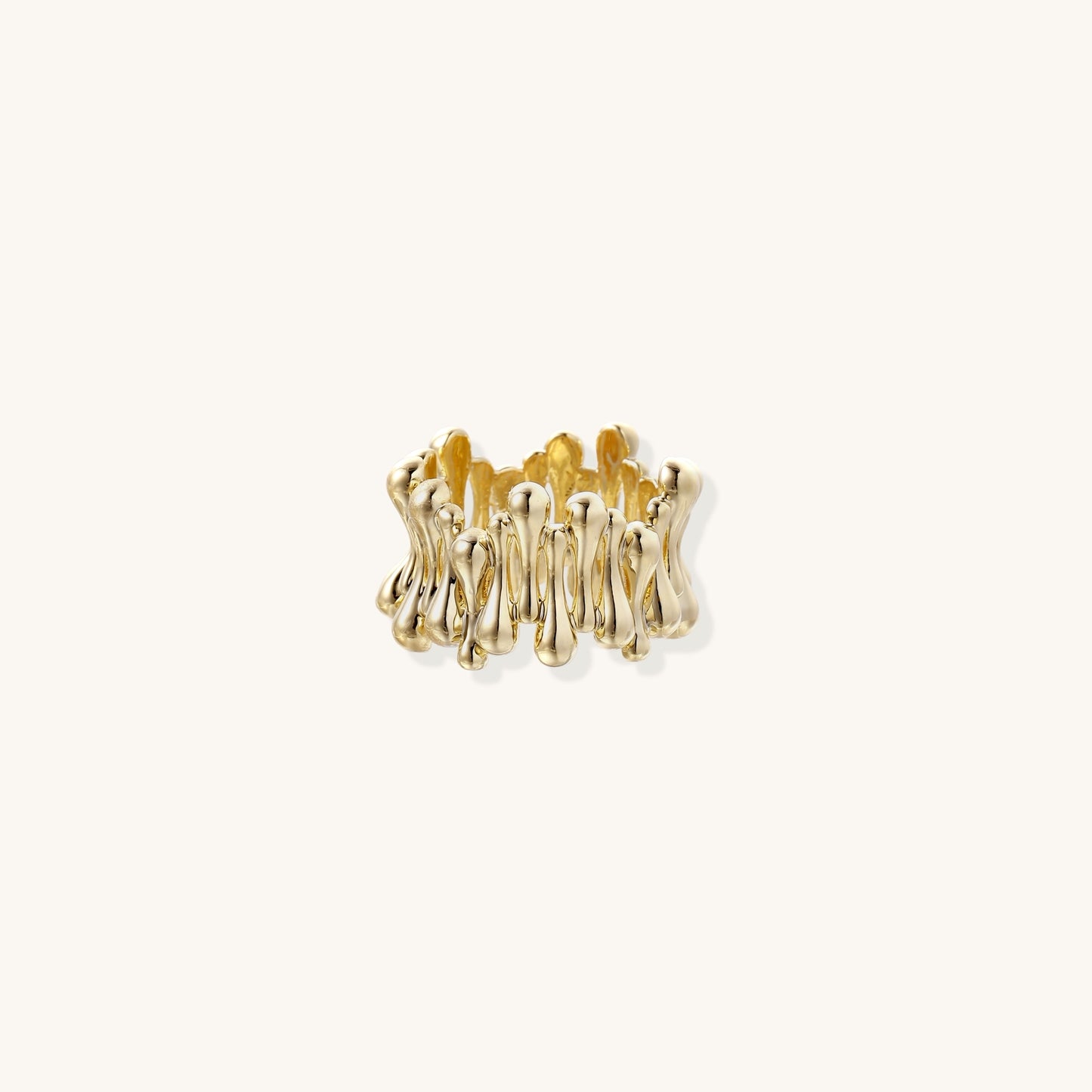 Close-up of chunky 18K gold-plated brass ring with flowing wave-like sculptural design on neutral background.
