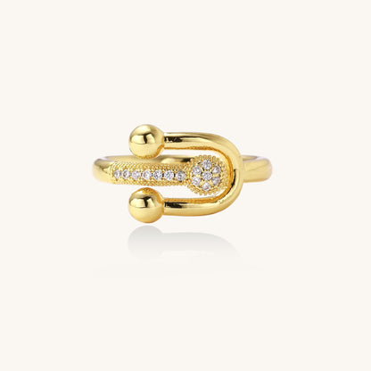 Modern gold-plated adjustable ring with safety pin design and sparkling cubic zirconia accents on white background