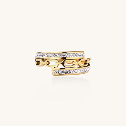 Gold-plated chain-link ring with rhinestone rows on cream background, showing bold geometric design and sparkling details.