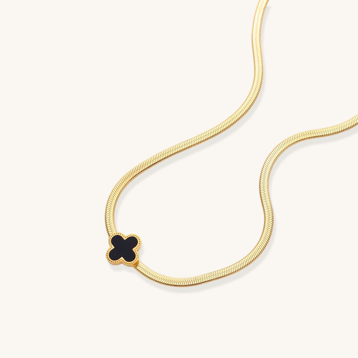 Delicate gold-plated chain necklace featuring a black quatrefoil clover pendant on white background.
