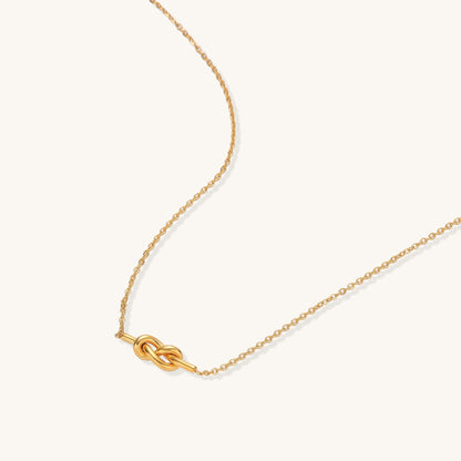Dainty 18K gold plated stainless steel chain necklace with minimalist knot pendant on cream background.