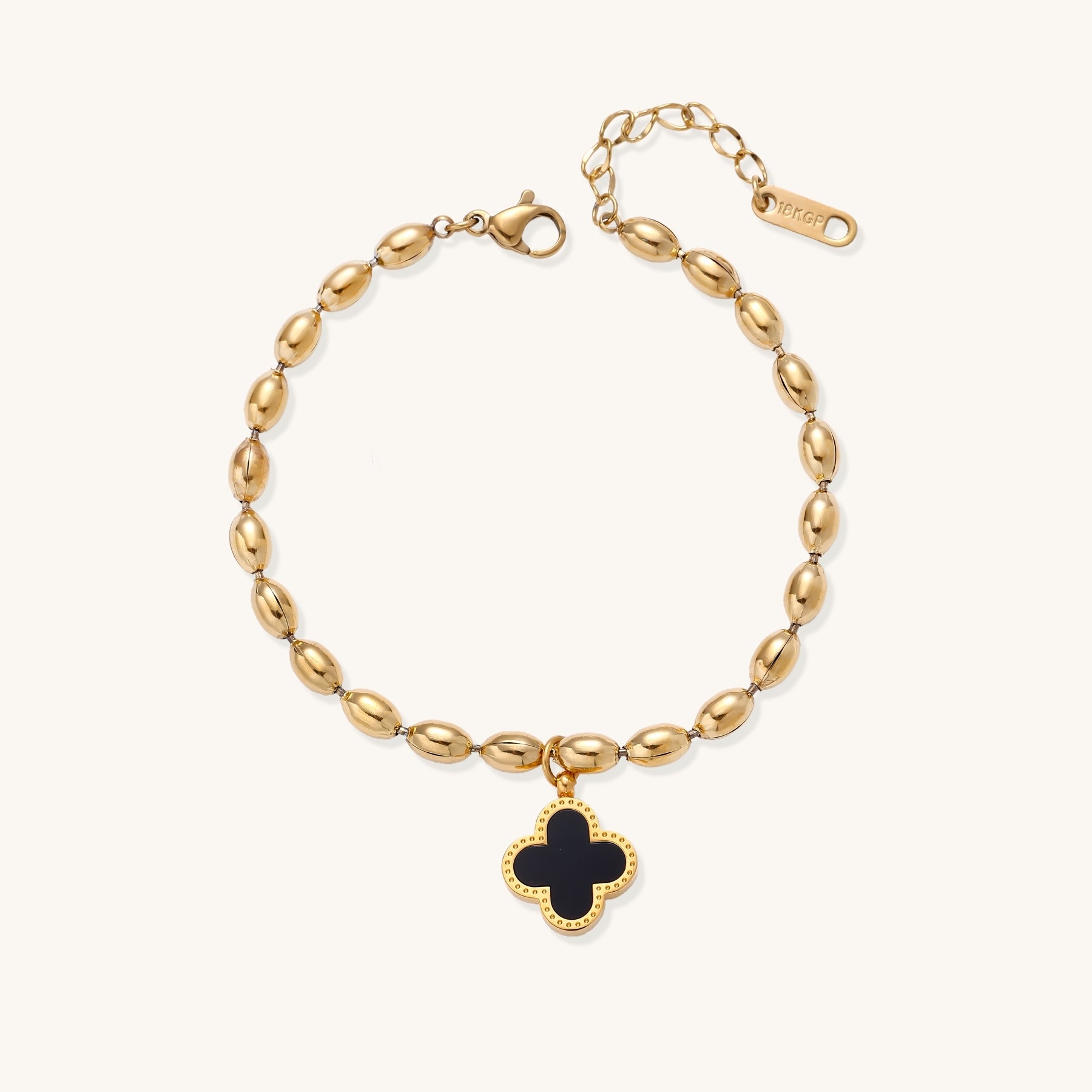 Dainty gold-plated beaded bracelet with oval links and four-leaf clover charm pendant on neutral background.