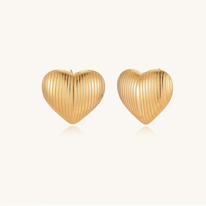 Close-up of ridged heart-shaped gold-plated stud earrings with textured surface pattern on cream background.