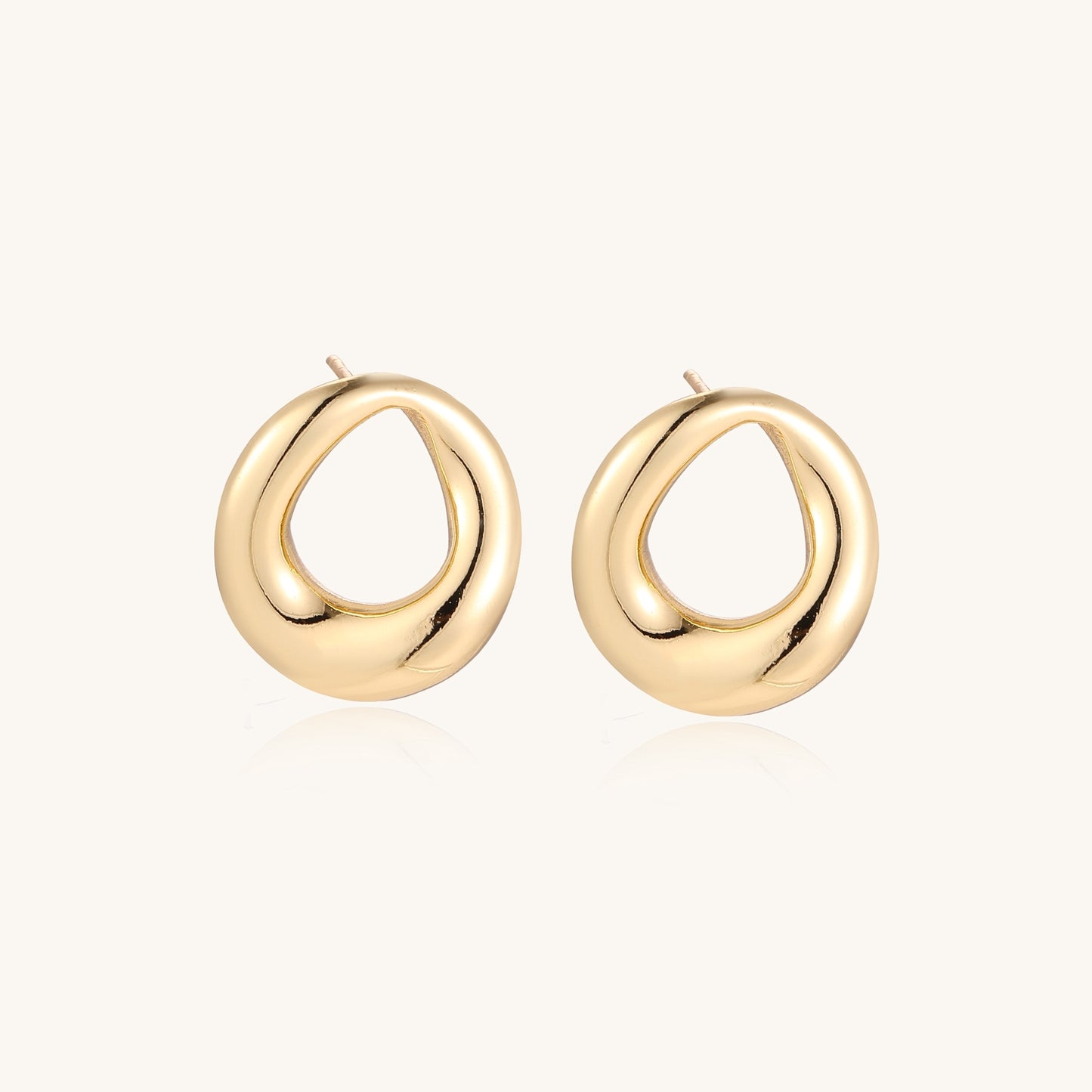 Pair of polished 18K gold-plated stainless steel oval loop stud earrings on cream background