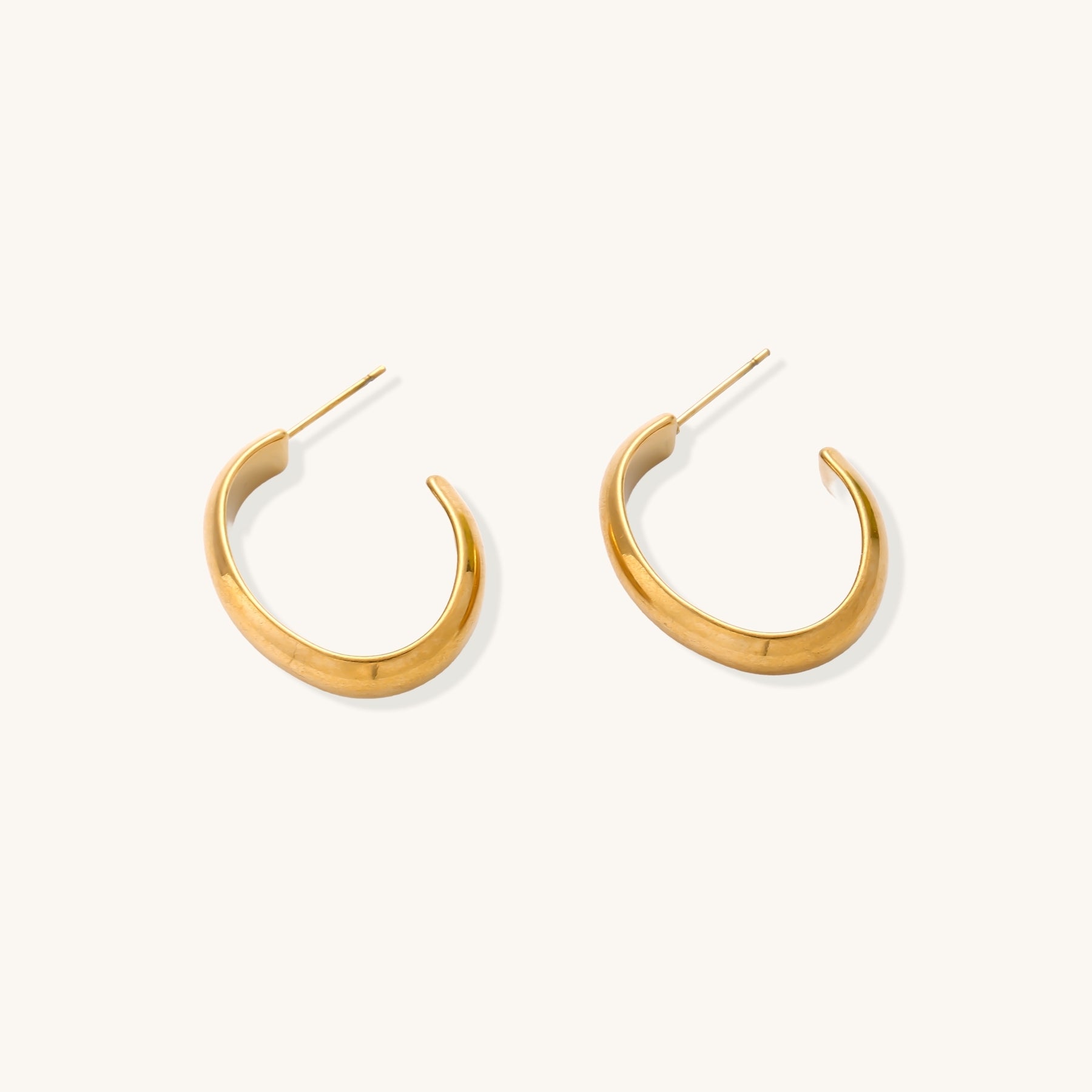 Four pairs of gold-plated stainless steel earrings including hoops and studs displayed on cream background