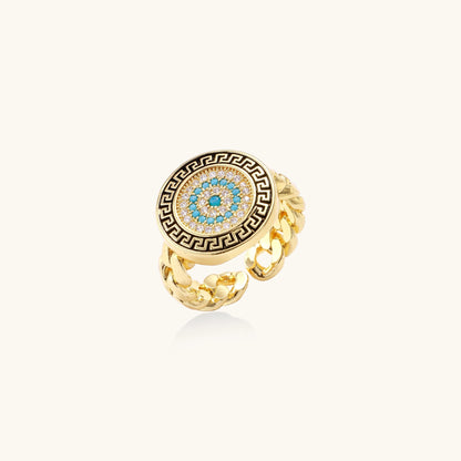 Gold-plated brass ring with Greek key border, evil eye center, and turquoise cubic zirconia stones in chunky chain band style.