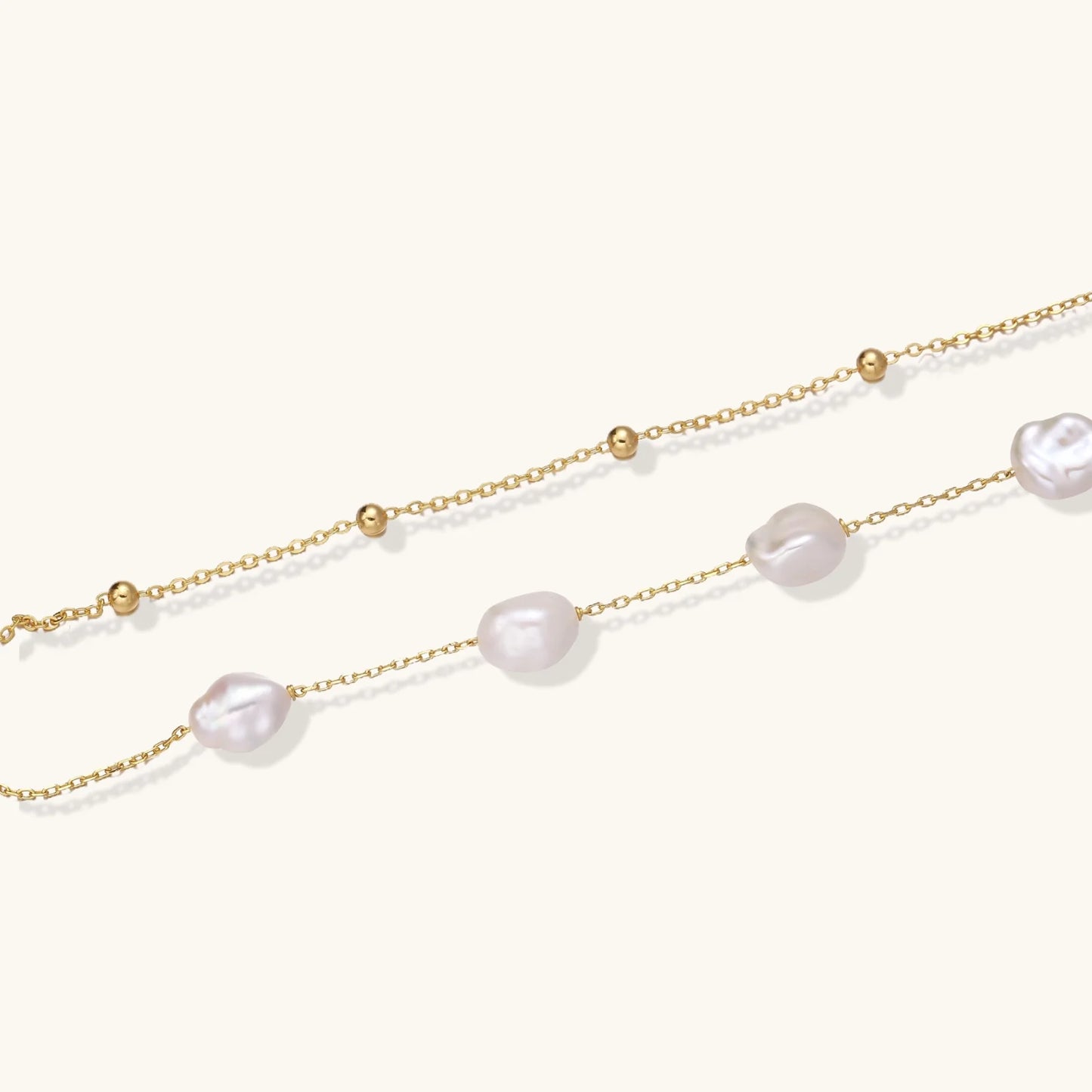 Double-strand gold bracelet with irregular baroque pearls and smooth freshwater pearls on cream background.