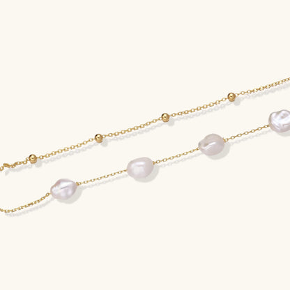 Double-strand gold bracelet with irregular baroque pearls and smooth freshwater pearls on cream background.