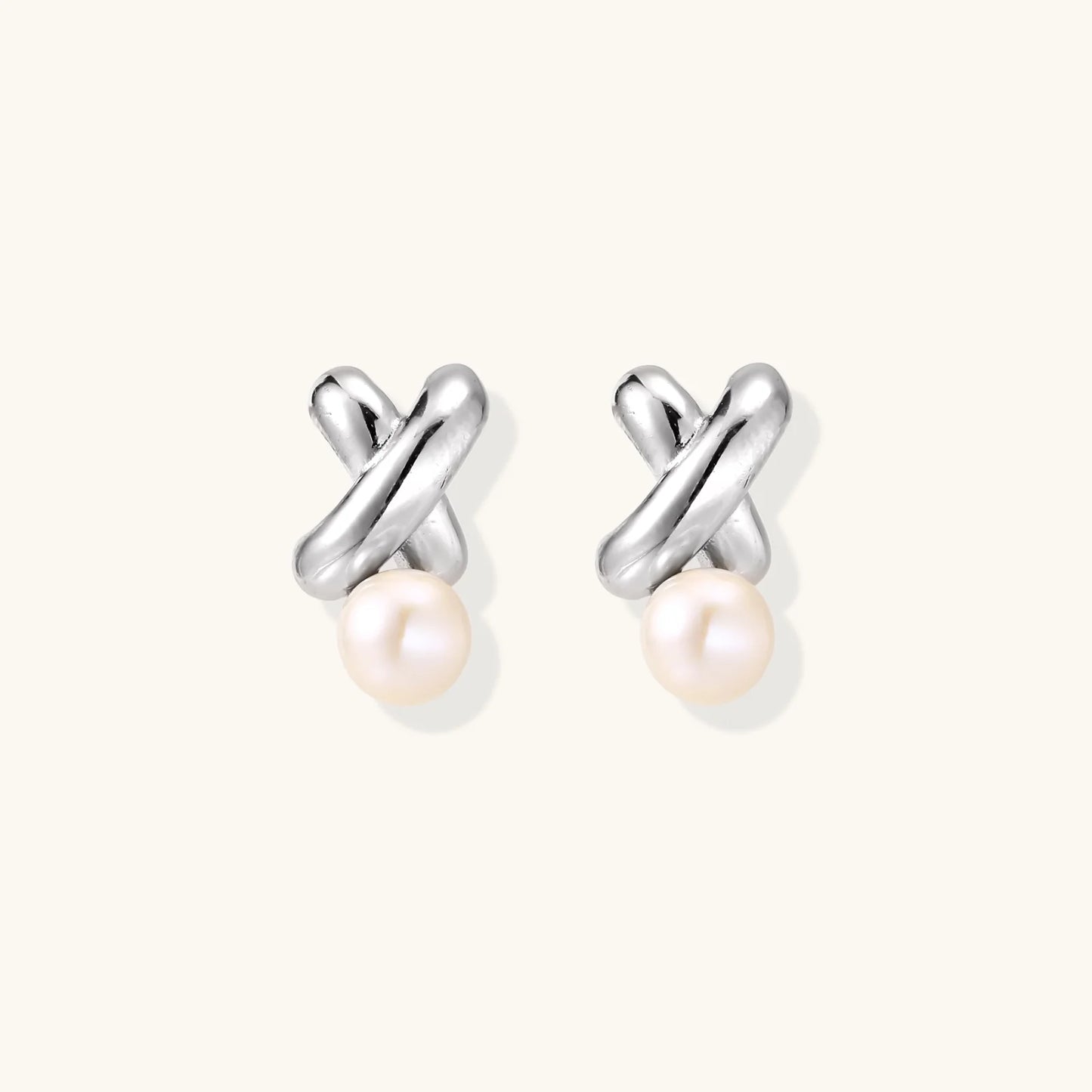 Rhodium-plated silver earrings with twisted X design and freshwater pearl drops on beige background