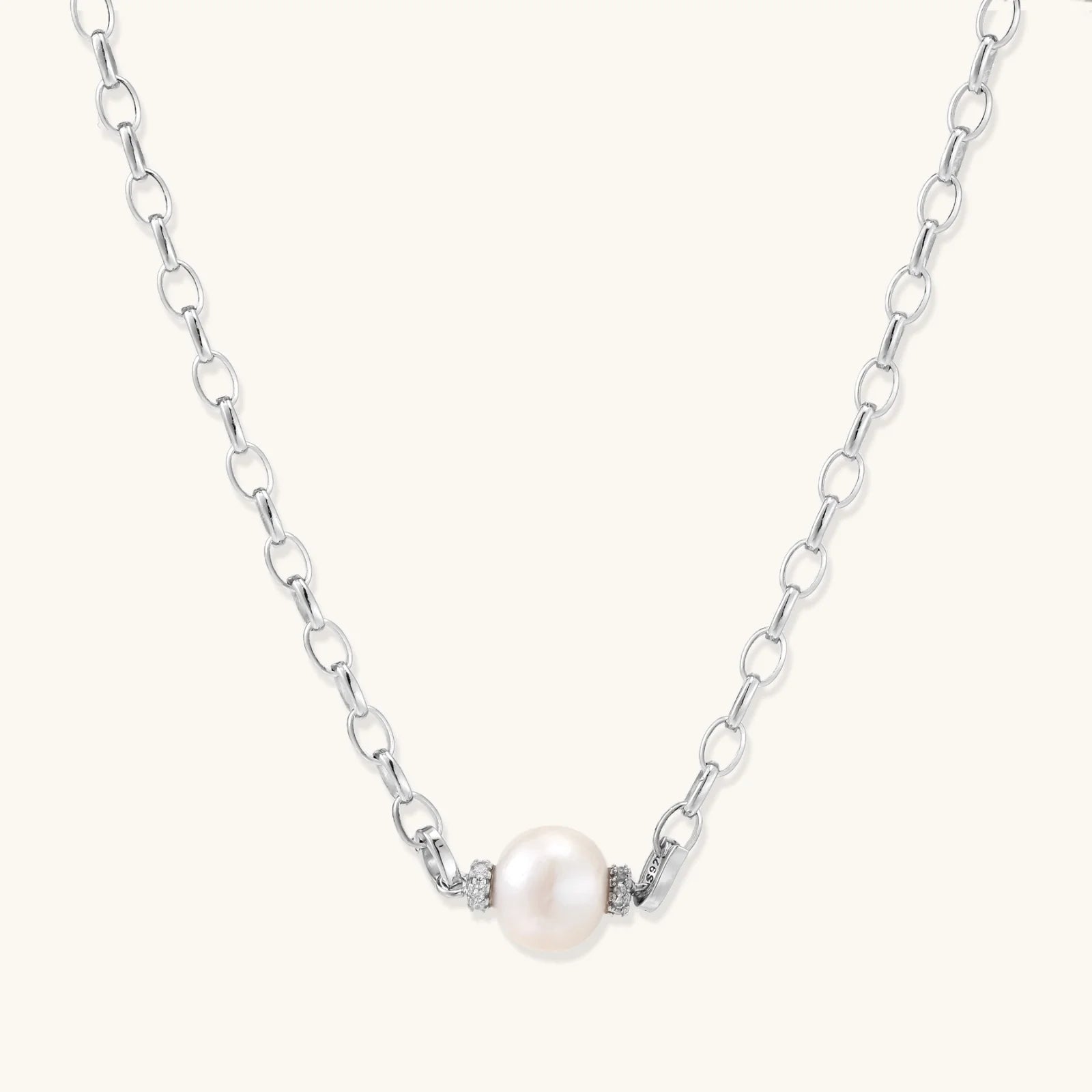 Dainty rhodium-plated silver chain necklace with centered 10mm freshwater pearl and crystal accents on cream background