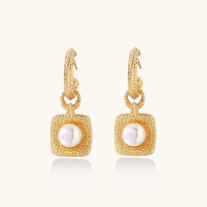 Pair of gold vermeil hoop earrings with textured square frames holding freshwater pearls on cream background
