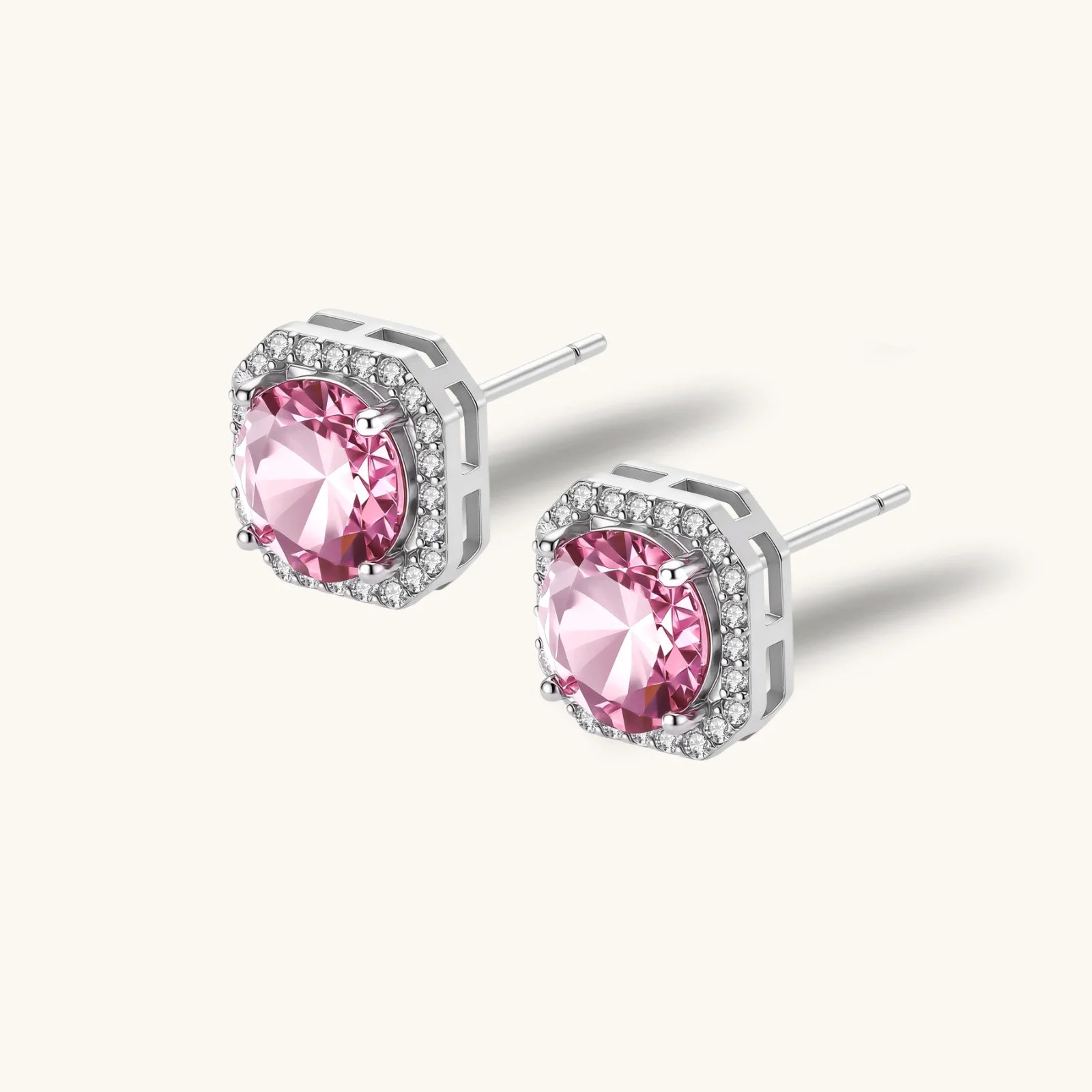 Pink moissanite studs in octagonal sterling silver halo settings with sparkling accent stones on cream background.