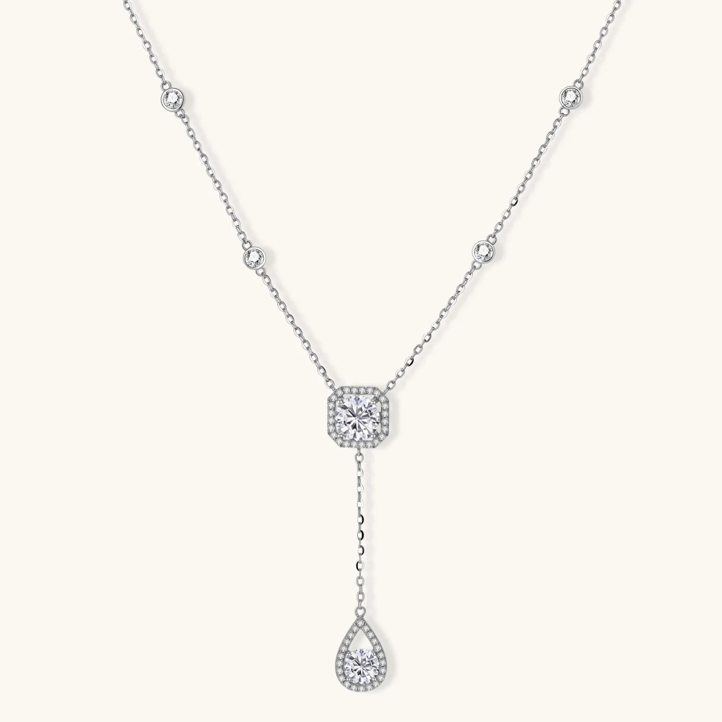Sterling silver necklace with cushion-cut moissanite in halo setting and teardrop pendant, displayed on cream background.
