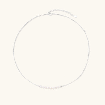 Delicate sterling silver chain necklace with small freshwater pearls arranged in a curved smile arc on cream background.