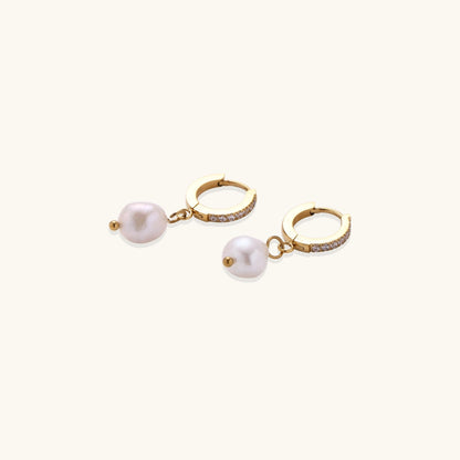 Gold huggie hoop earrings with pavé crystals and white freshwater pearl drops on cream background
