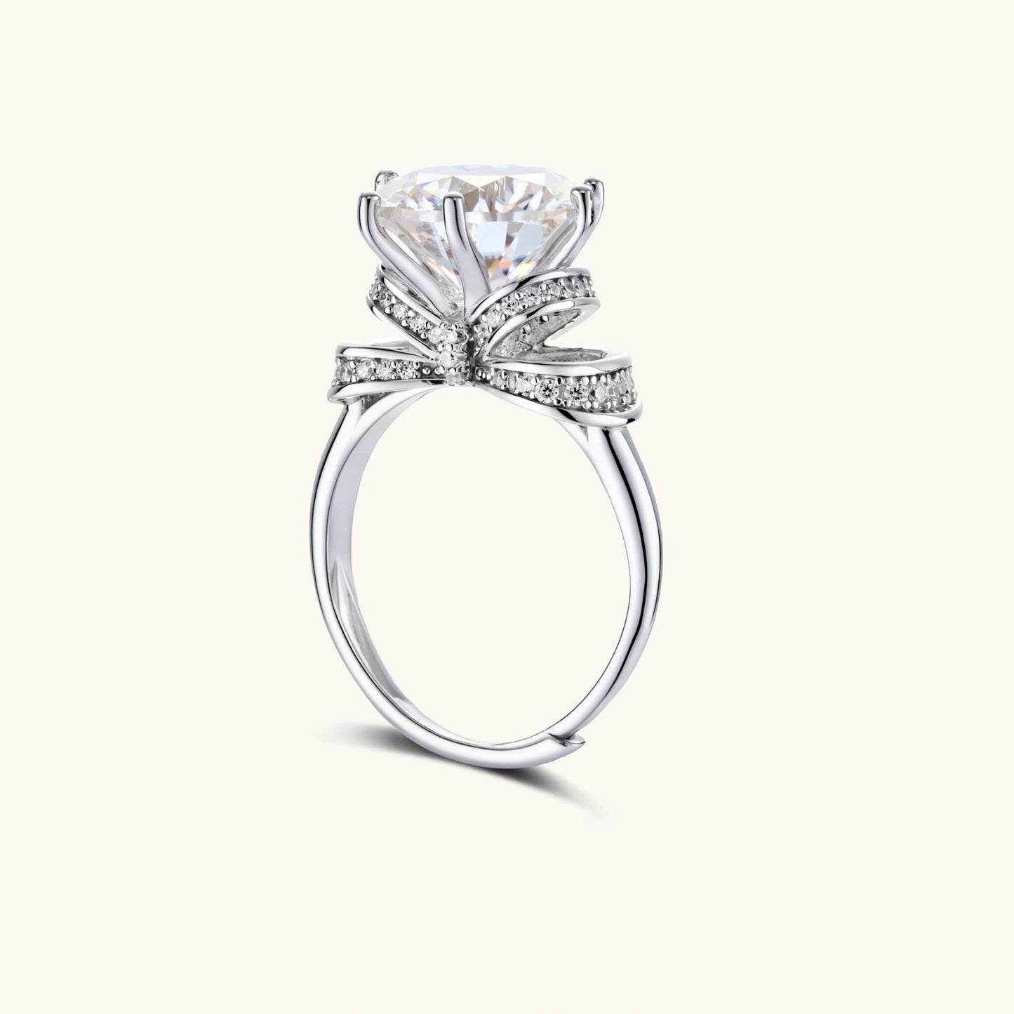 Sterling silver ring with 5ct round moissanite center stone and intricate bow design with pavé accents on white background.