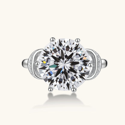 Sterling silver ring with 5ct round moissanite center stone and intricate bow design with pavé accents on white background.