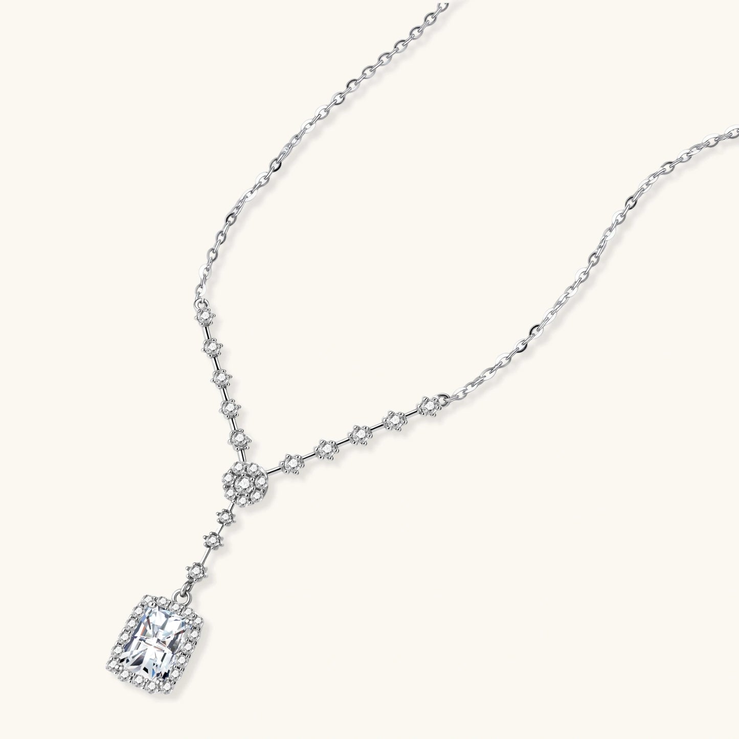 Sterling silver Y-necklace with rectangular moissanite pendant in halo setting and cascading accent stones on white background.