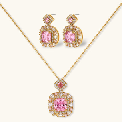Ornate gold-plated jewelry set with rose pink zirconia center stones and crystal accents on cream background.